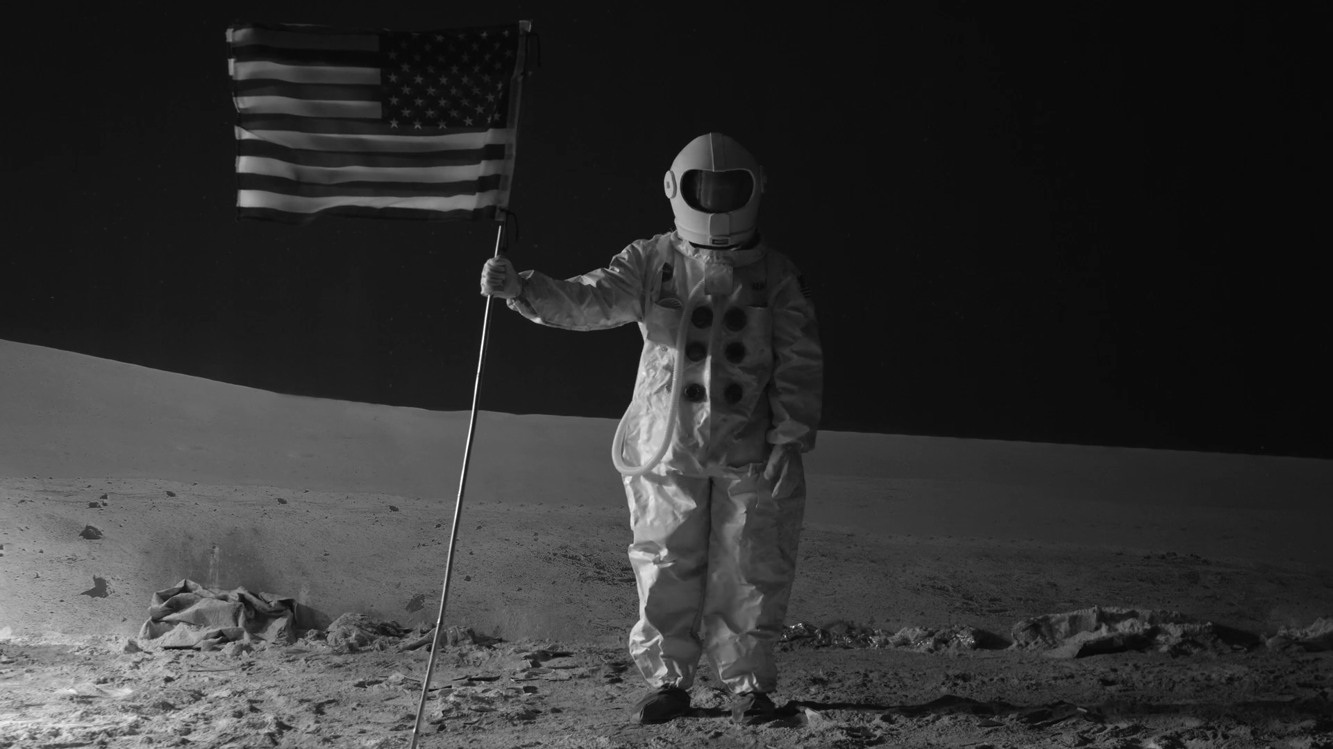 Black-and-white scene of an astronaut holding a flag on a lunar set