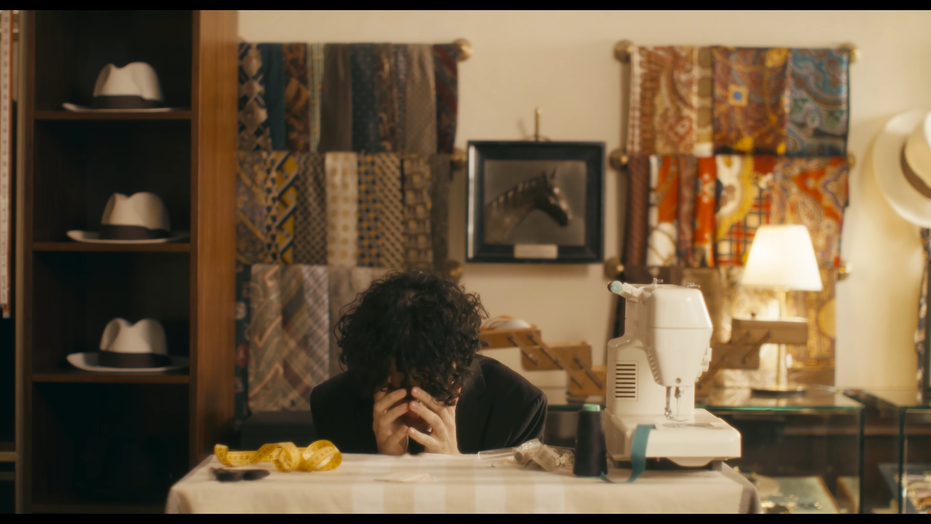 Man sitting at a sewing table with his hands to his face