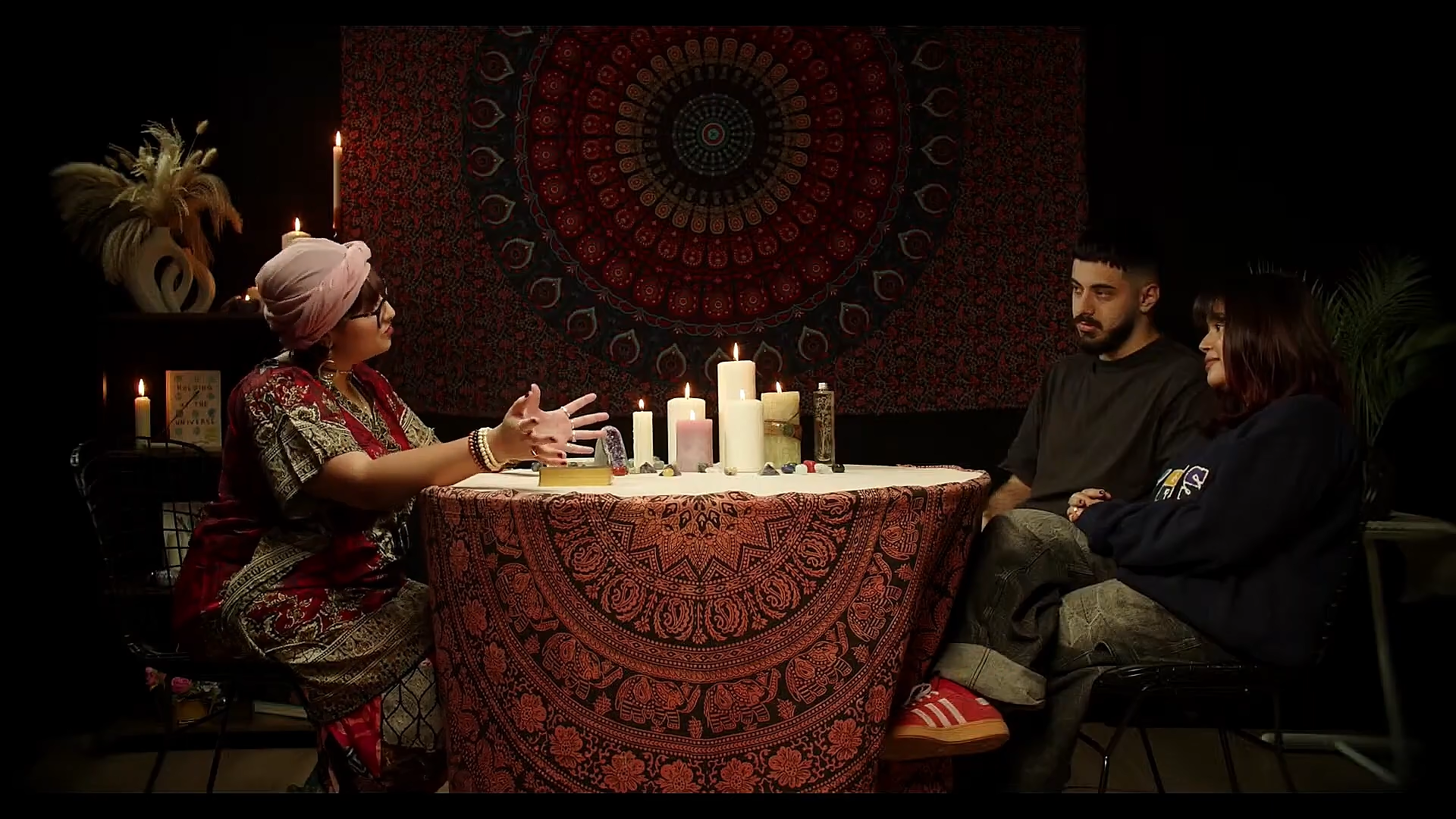Three presenters seated at a table against mandala patterns