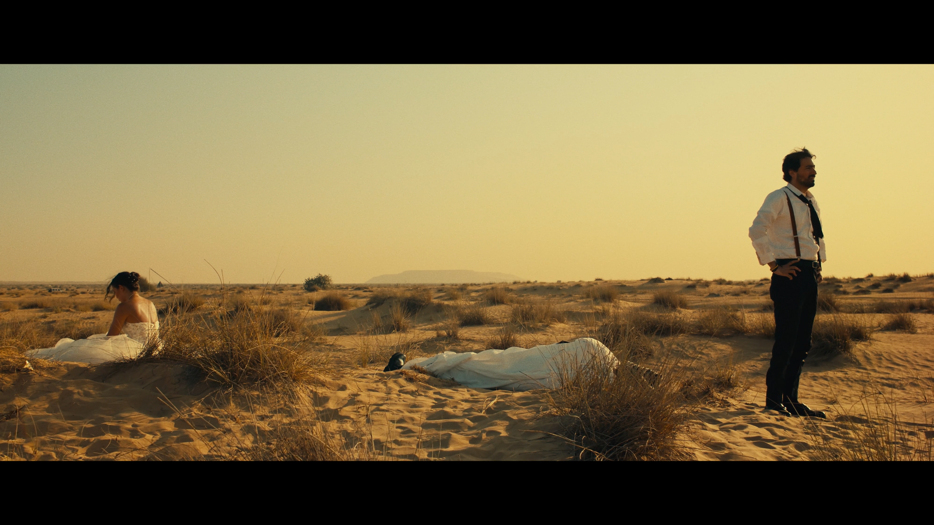 Bride and groom separated by a covered figure in the desert